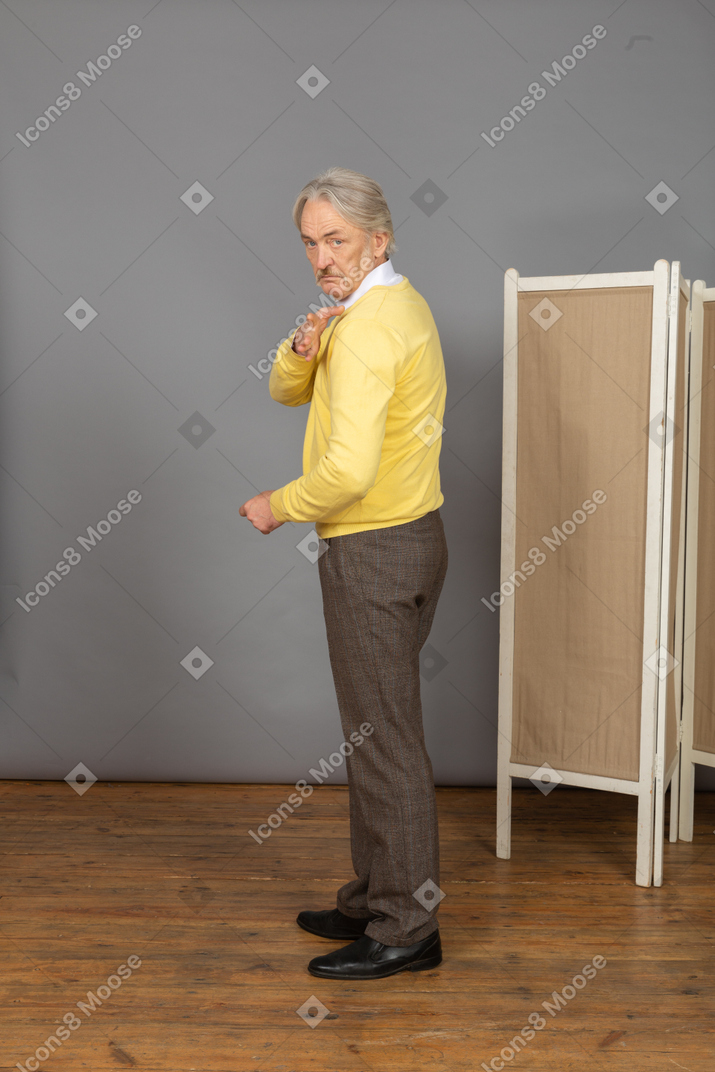 Вид сбоку старика, смотрящего в камеру, касаясь плеча