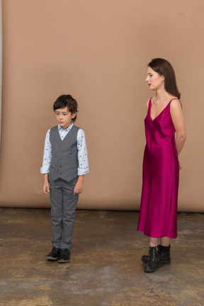Mujer en vestido rojo sosteniendo los brazos detrás de la espalda mientras el niño está parado cerca de ella