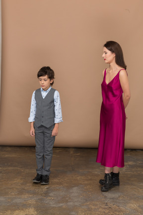 Woman in red dress holding arms behind back while boy standing near her