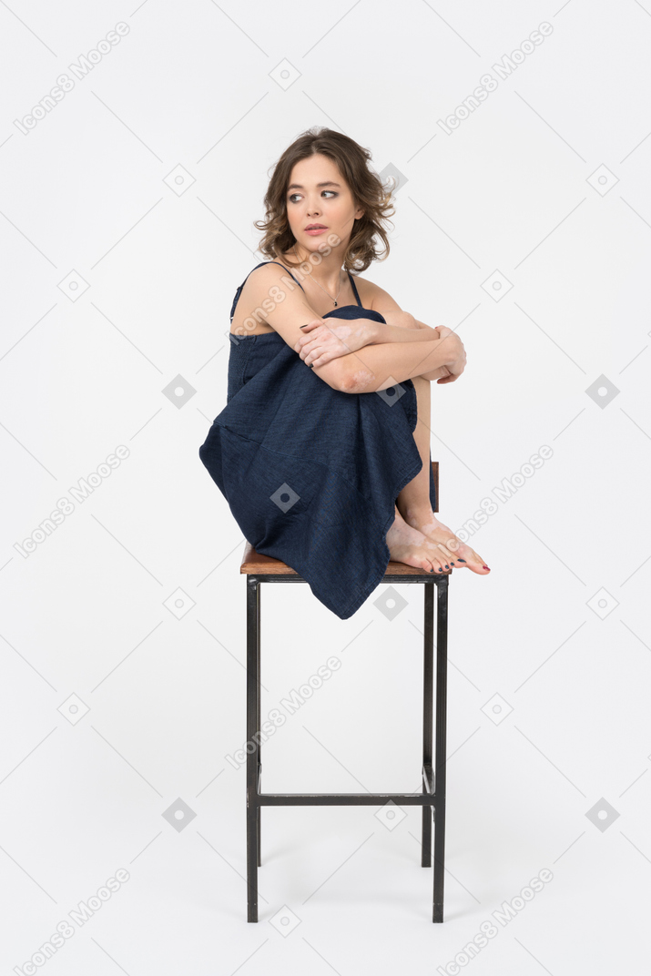 Woman sitting on a bar chair with her legs tucked