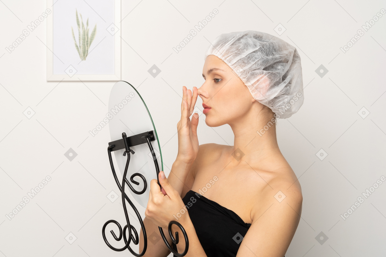 Young woman in surgical cap lifting her nose while looking in the mirror