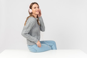 Mujer joven sentada en la mesa y escuchando música en auriculares