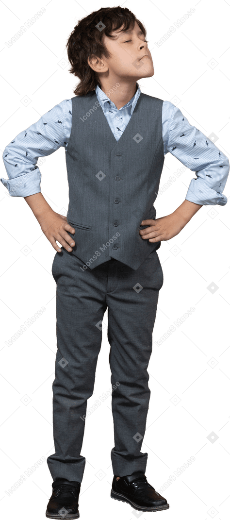 Front view of a cute boy in grey suit posing with hands on hips and looking up
