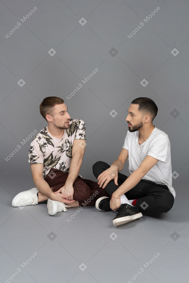 床に座って話している2人の若い男性