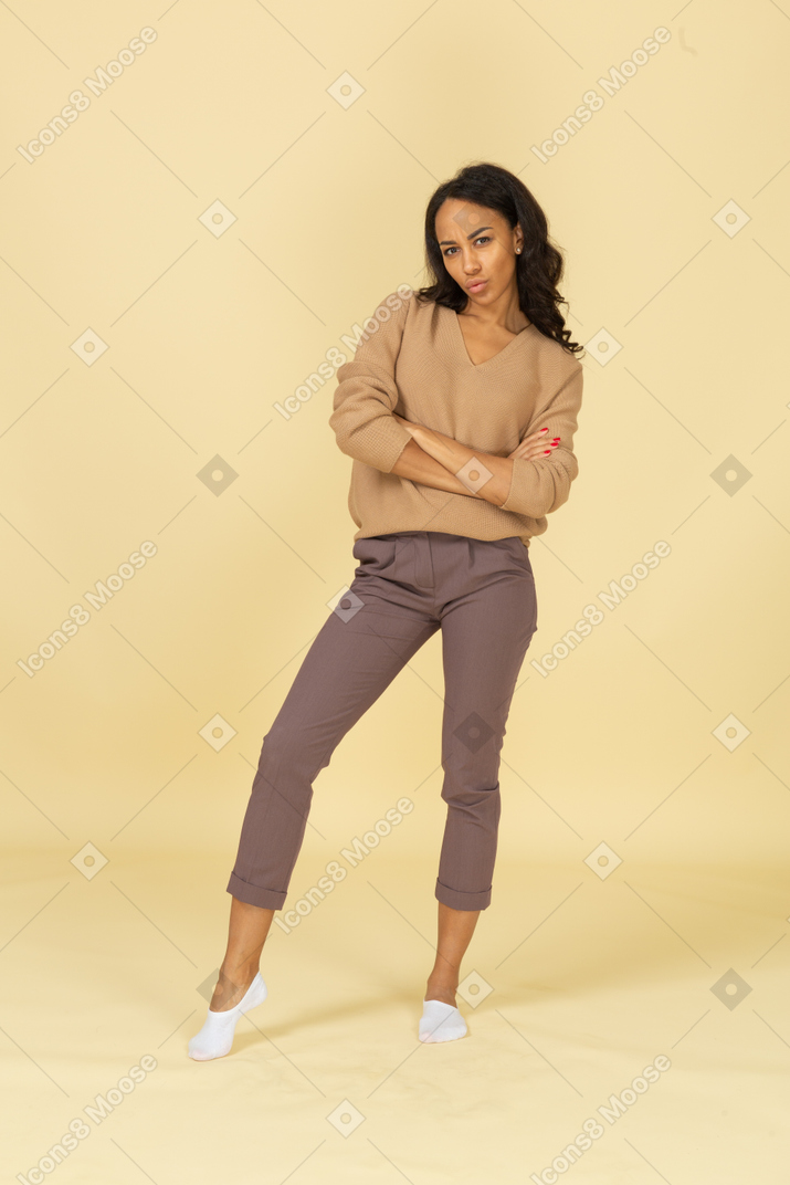 Vista frontal de una mujer joven de piel oscura haciendo pucheros cruzando los brazos
