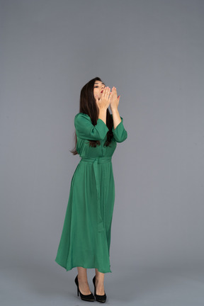 Vue de trois quarts d'une jeune femme en robe verte envoyant un baiser aérien