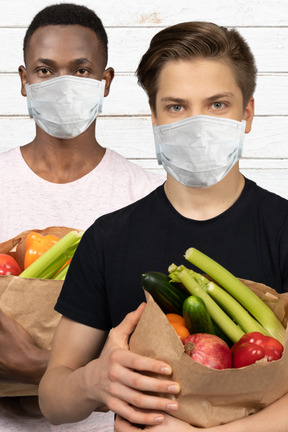 Two men wearing face masks holding grocery bags