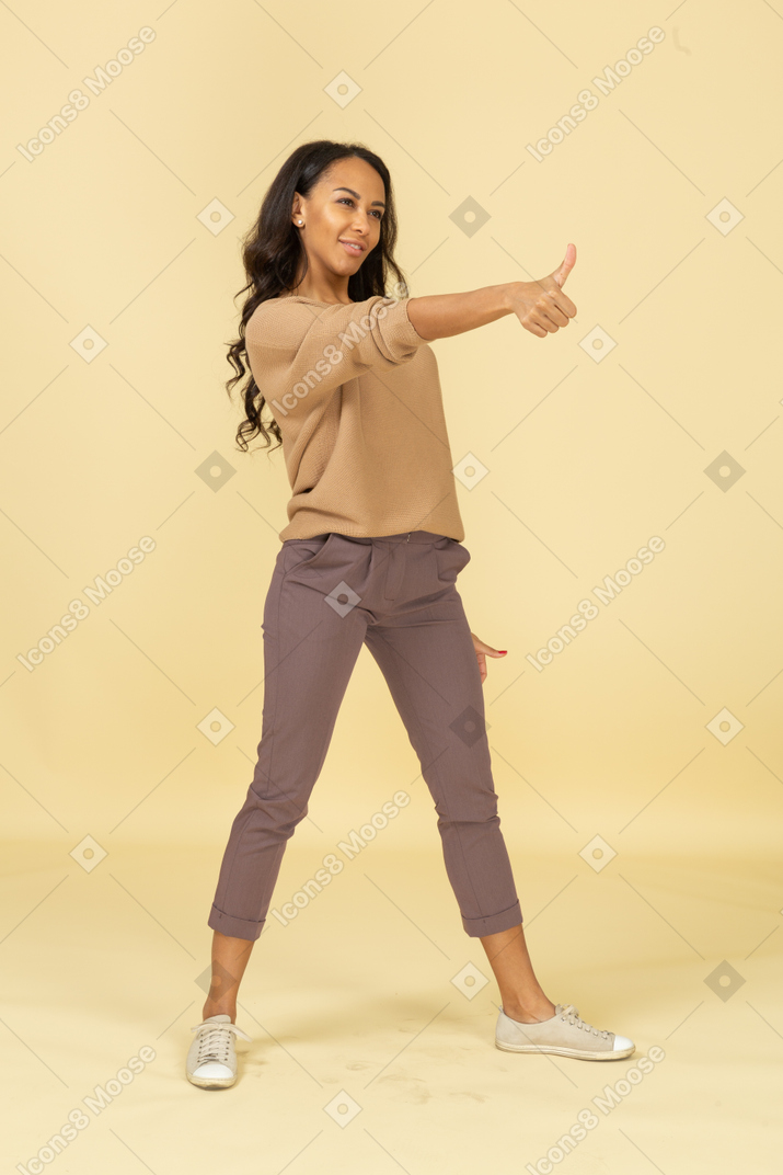Трехчетвертный вид довольной темнокожей молодой женщины, показывающей большой палец вверх