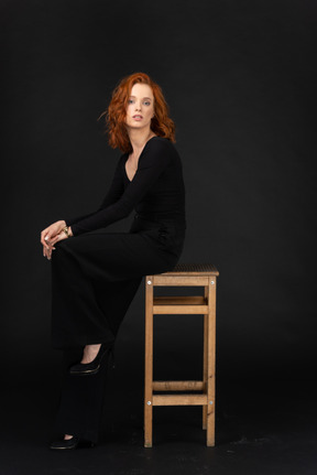 A side view of the cute woman sitting on the wooden chair and dressed in black