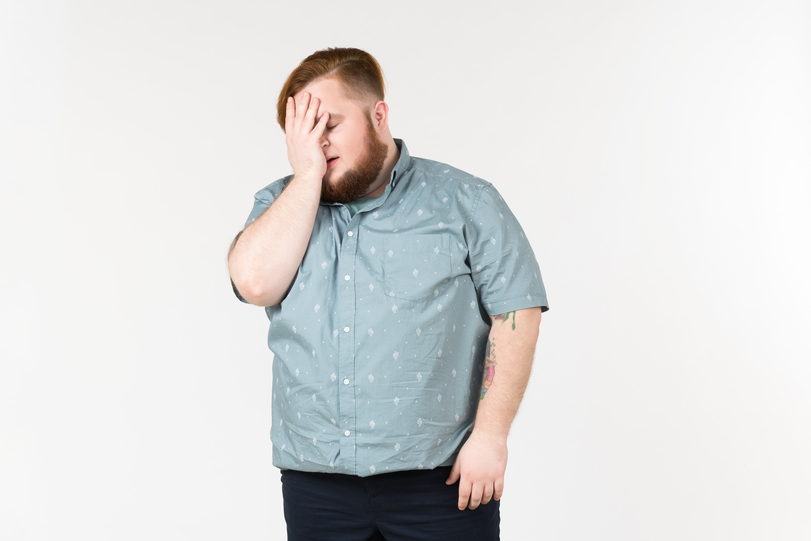 Confused looking young overweight man closing his face with a hand