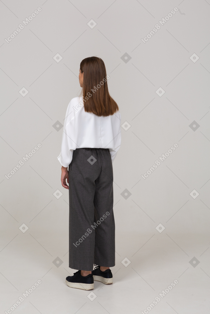 Vue de trois quarts arrière d'une jeune femme en tenue de bureau regardant de côté
