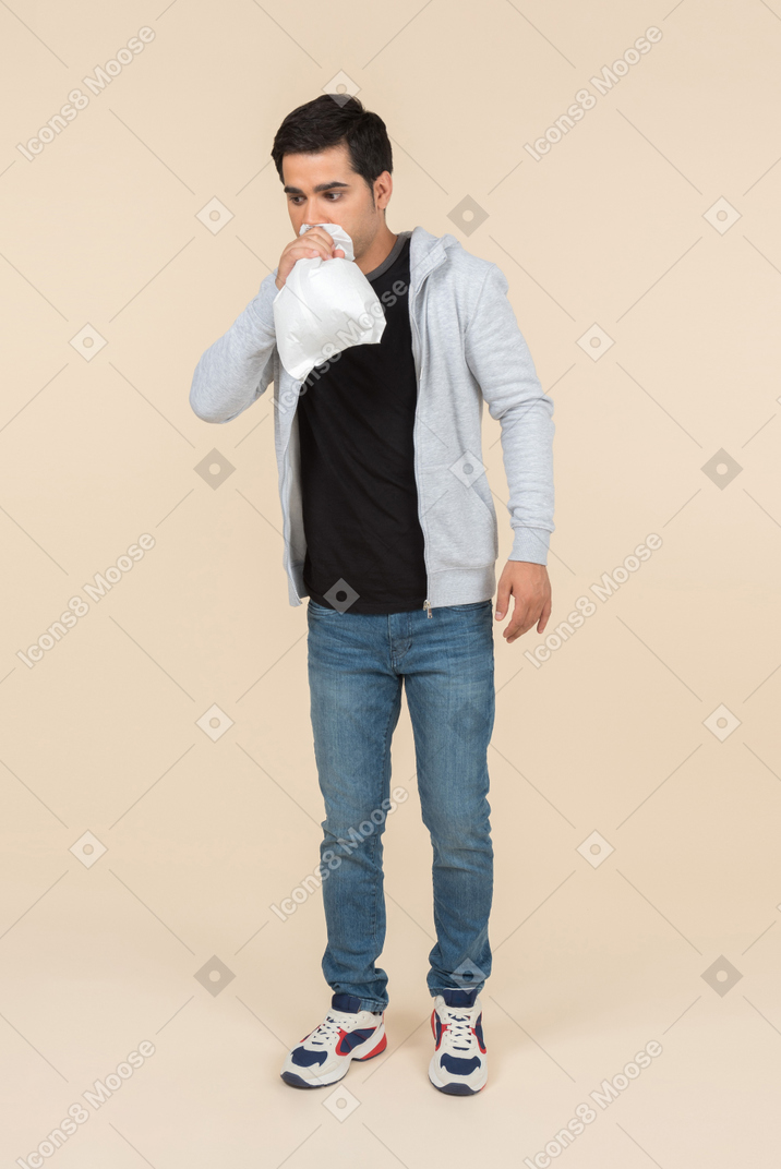 Jovem homem caucasiano respirando em um saco de papel