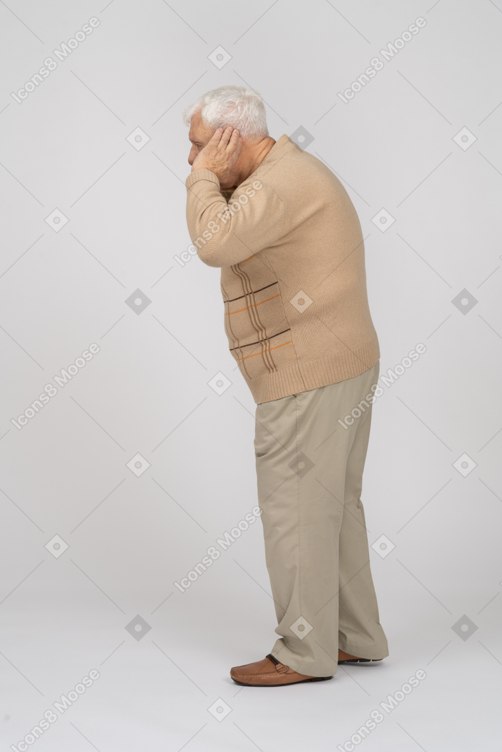 Vue latérale d'un vieil homme en vêtements décontractés tient la main à côté de l'oreille