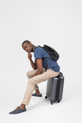 Pensive male tourist sitting on grey luggage