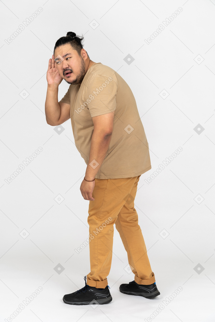 Annoyed asian man helping himself with his palm trying to hear something