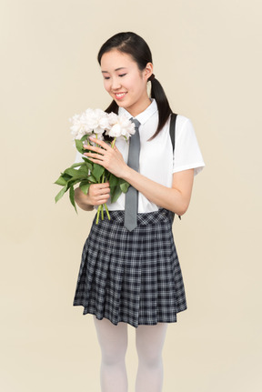 Menina da escola asiática olhando atentamente sobre flores