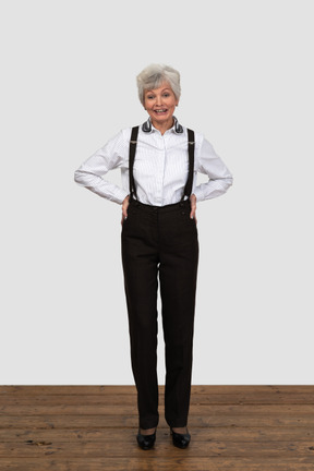 A smiling old woman dressed in trousers and suspenders smiling and putting hands in hips