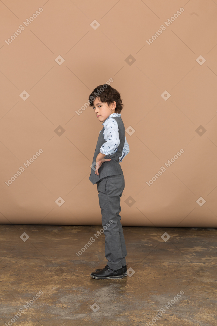 腰に手を置いて立っている灰色のスーツを着た少年の側面図