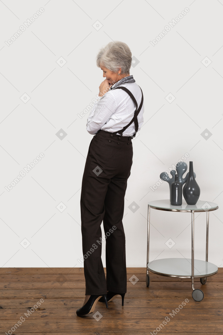 Three-quarter back view of a pleased old lady in office clothing holding hands together