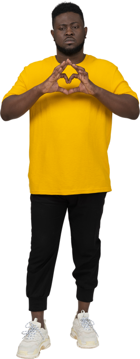 Vista frontal de um jovem sombrio de pele escura em uma camiseta amarela mostrando um gesto de coração