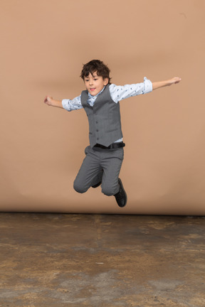 Вид спереди на симпатичного мальчика в костюме, прыгающего с вытянутыми руками