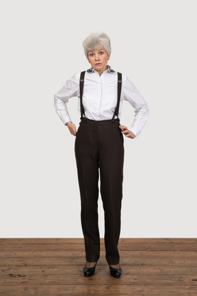 Vista frontal de una anciana disgustada en ropa de oficina poniendo las manos en las caderas