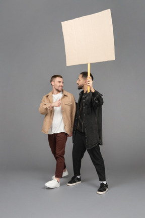 Vista di tre quarti di due giovani uomini che portano un cartellone pubblicitario e chiacchierano