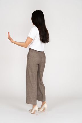 Vista posteriore di tre quarti di una giovane donna in calzoni che tende le mani