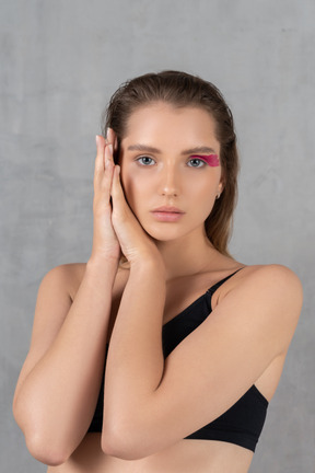 Portrait of a young woman with bright pink eye make-up holding hands next to cheek