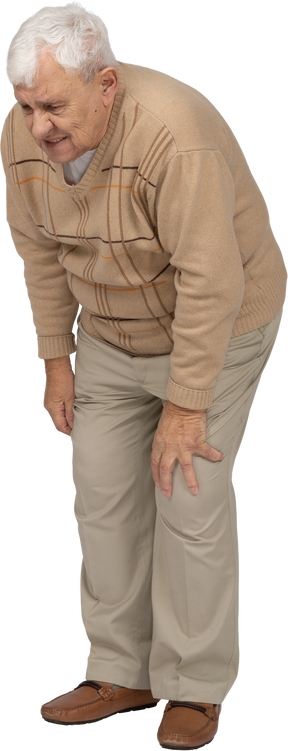 Вид спереди на старика в повседневной одежде, наклоняющегося и касающегося своего больного колена