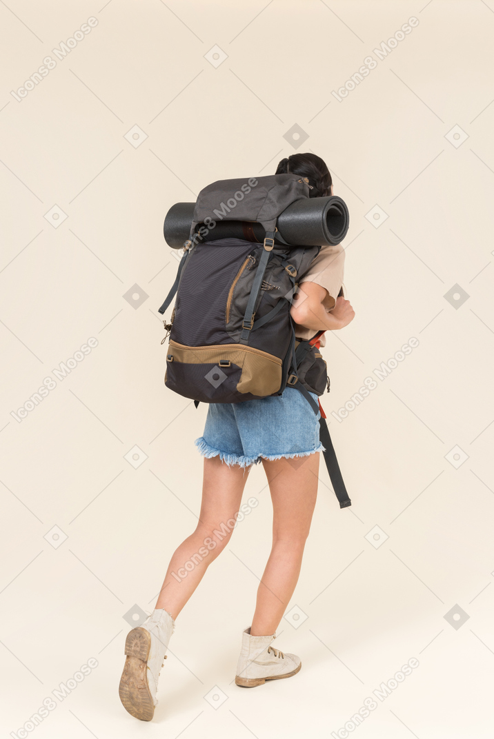 年轻女性的徒步旅行者携带沉重的背包和站回相机