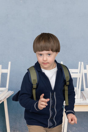 Kleiner junge mit rucksack, der in einem klassenzimmer steht