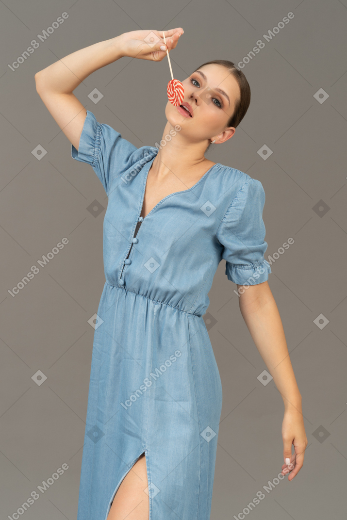 Vista de tres cuartos de una mujer joven en vestido azul sosteniendo una piruleta