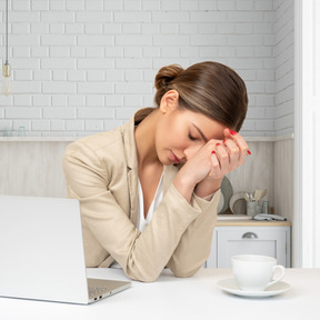 An exchausted woman sitting at a desk in front of a laptop