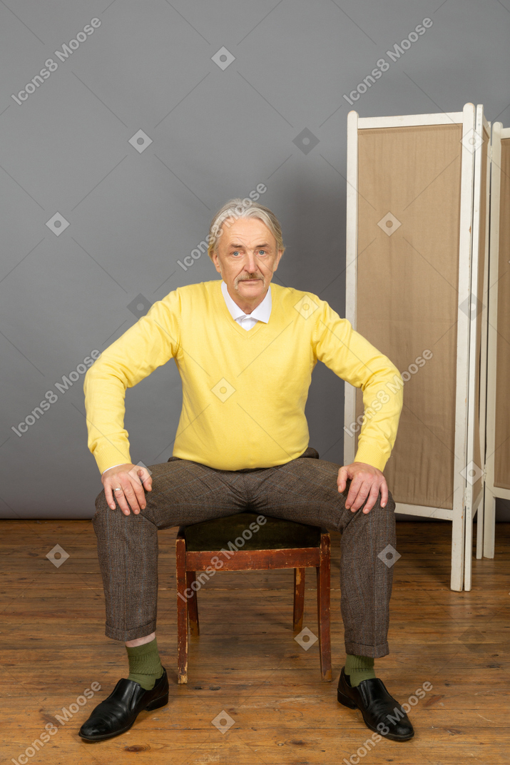 Man sitting with his legs spread wide apart and looking at camera
