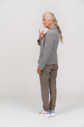 Vista traseira de uma senhora idosa de terno mostrando o sinal v