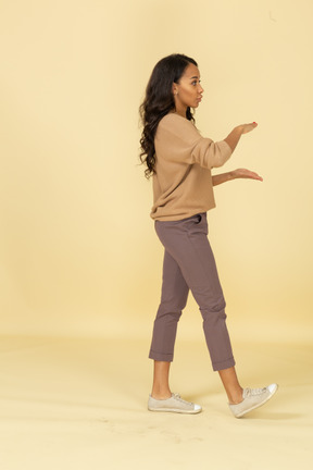 Vista lateral de una mujer joven de piel oscura que muestra el tamaño de algo