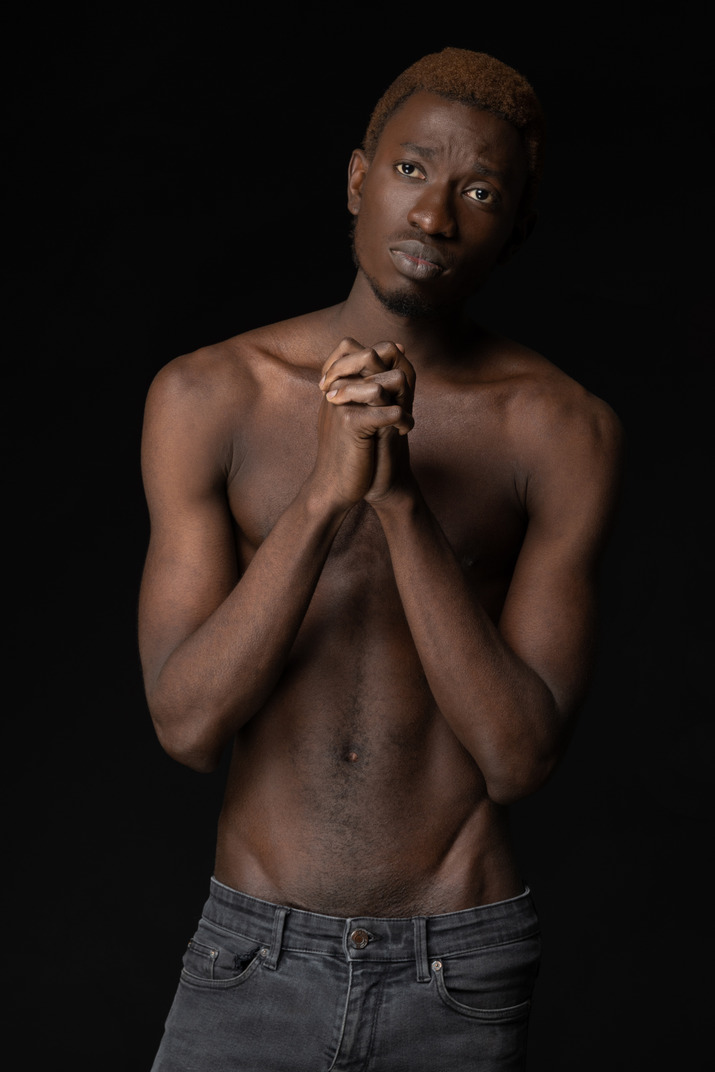 Afrikanischer junger mann auf einem schwarzen hintergrund, der hände zusammenstellt