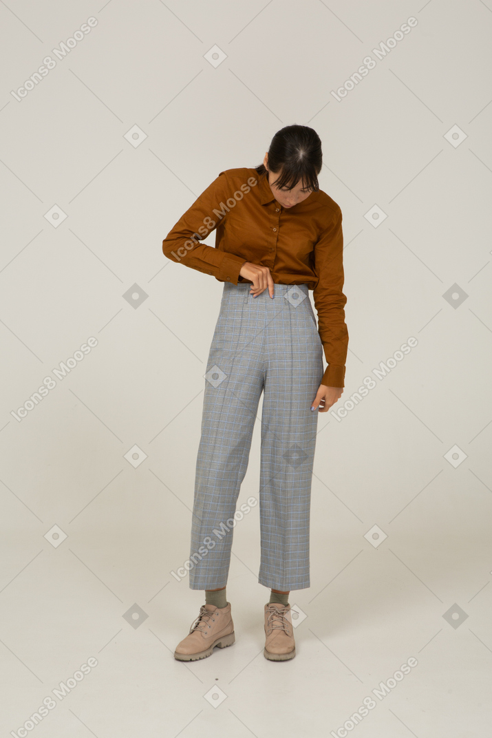 Front view of a young asian female in breeches and blouse touching trousers and looking down