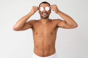 Jovem barechested cobrindo os olhos com almofadas de algodão