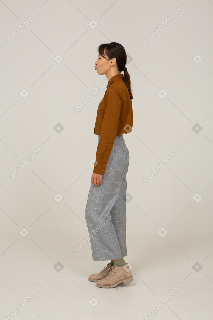 Vista lateral de uma jovem mulher asiática safada fazendo beicinho de calça e blusa