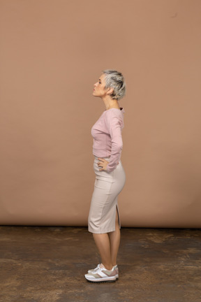 Женщина в повседневной одежде, стоя в профиль с руками в бедрах