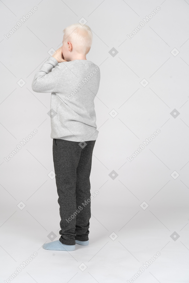 Vista posteriore di tre quarti di un ragazzo che si copre la bocca con le mani