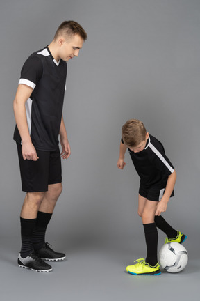 Full-length of a young man coaching little boy how to play fooyball