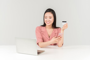 Sorrindo jovem mulher asiática segurando o cartão do banco ao fazer compras on-line