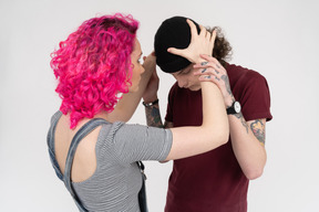 Pink-haired girl putting black hat on her boyfriend