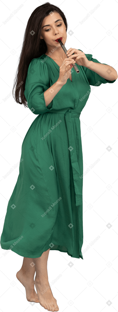 フルートを演奏する緑のドレスを着て歩く若い女性の4分の3のビュー