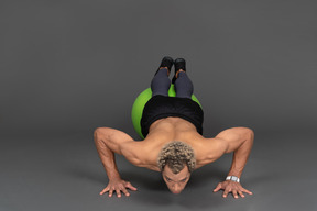 Front view of a shirtless afro man making push-ups on a gym ball