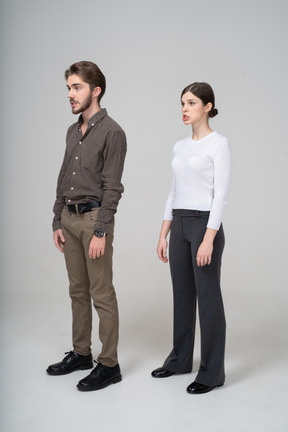 Vue de trois quarts d'un jeune couple grimaçant en vêtements de bureau