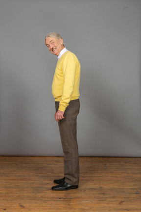 Side view of an old cheerful man in yellow pullover smiling and looking at camera